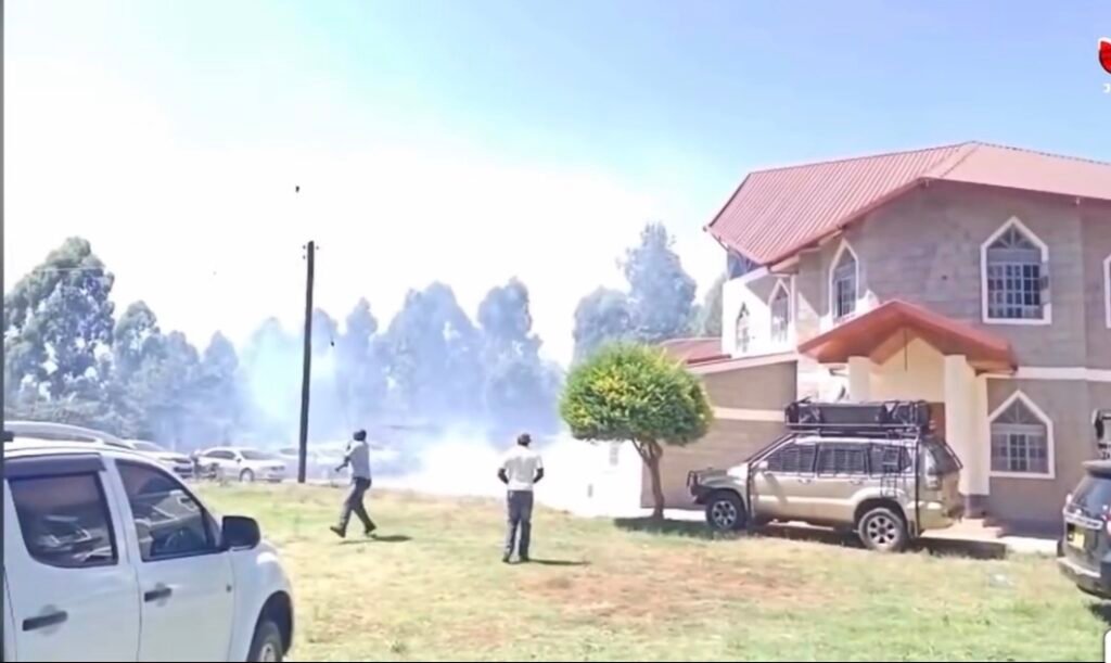 White teargas smoke engulfs ACK Witima Church in Othaya, Nyeri County, as a local lady aids worshippers affected by the attack.