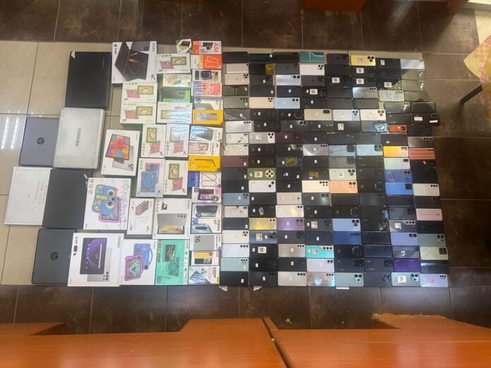 DCI officers display recovered stolen phones, tablets, and laptops seized in Nairobi operation targeting cross-border electronics trafficking.