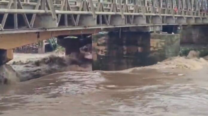 The Migori footbridge stands damaged as wild floodwaters rush beneath it following heavy rains.
