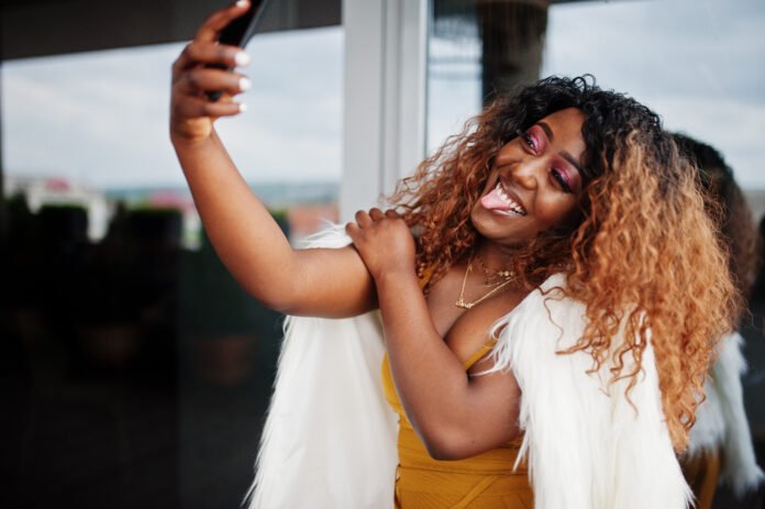 Glamour african american woman in yellow dress and white woolen Lady taking a selfie Courtesy/Freepik