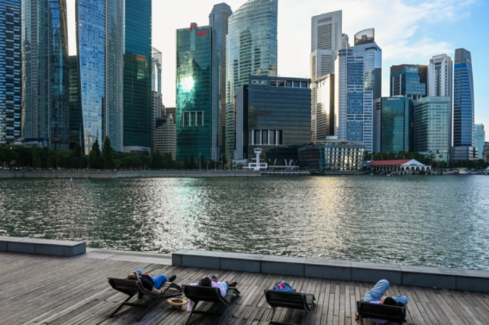 People relax on beach chairs along the boardwalk during sunset at Marina Bay in Singapore on February 9, 2026.
