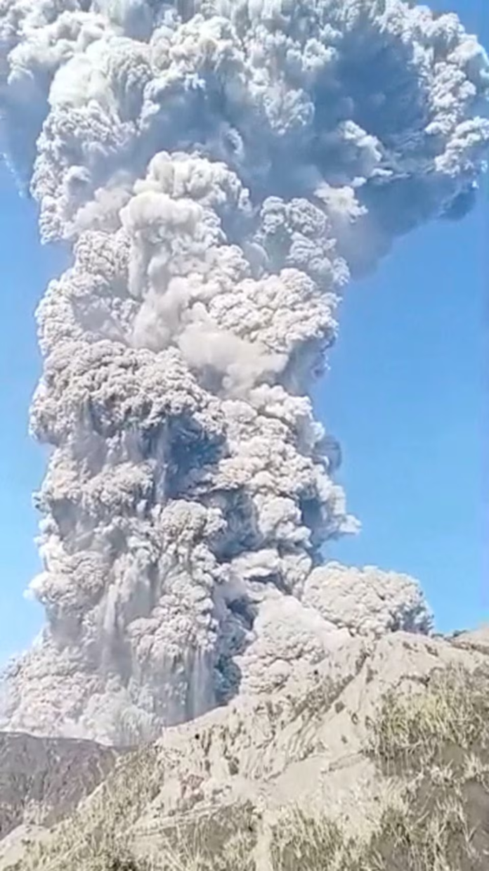 A massive column of ash and smoke spewing 10km into the sky from the crater of Indonesia's Mount Dukono, as captured during the May 2026 eruption, viewed from a distance on Halmahera island